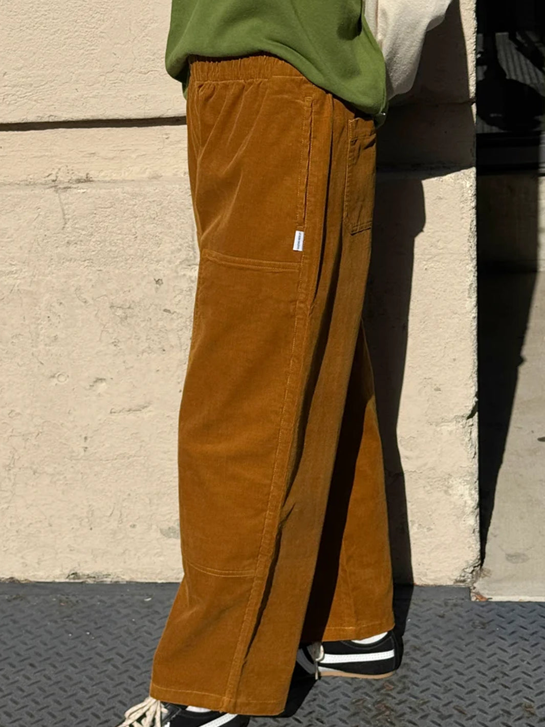Side view of Le Bon Shoppe Corduroy Gardener's Pants in Whiskey, styled with a green sweatshirt and black sneakers, highlighting the relaxed silhouette and utility-inspired details | Twentyseven Toronto