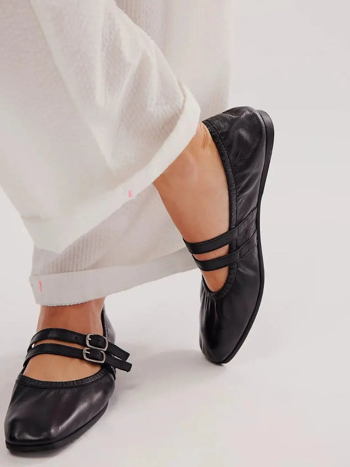 A model lifts one foot to display the sleek design and dual top straps of the Free People Gemini Ballet Flats - Black | Twentyseven Toronto
