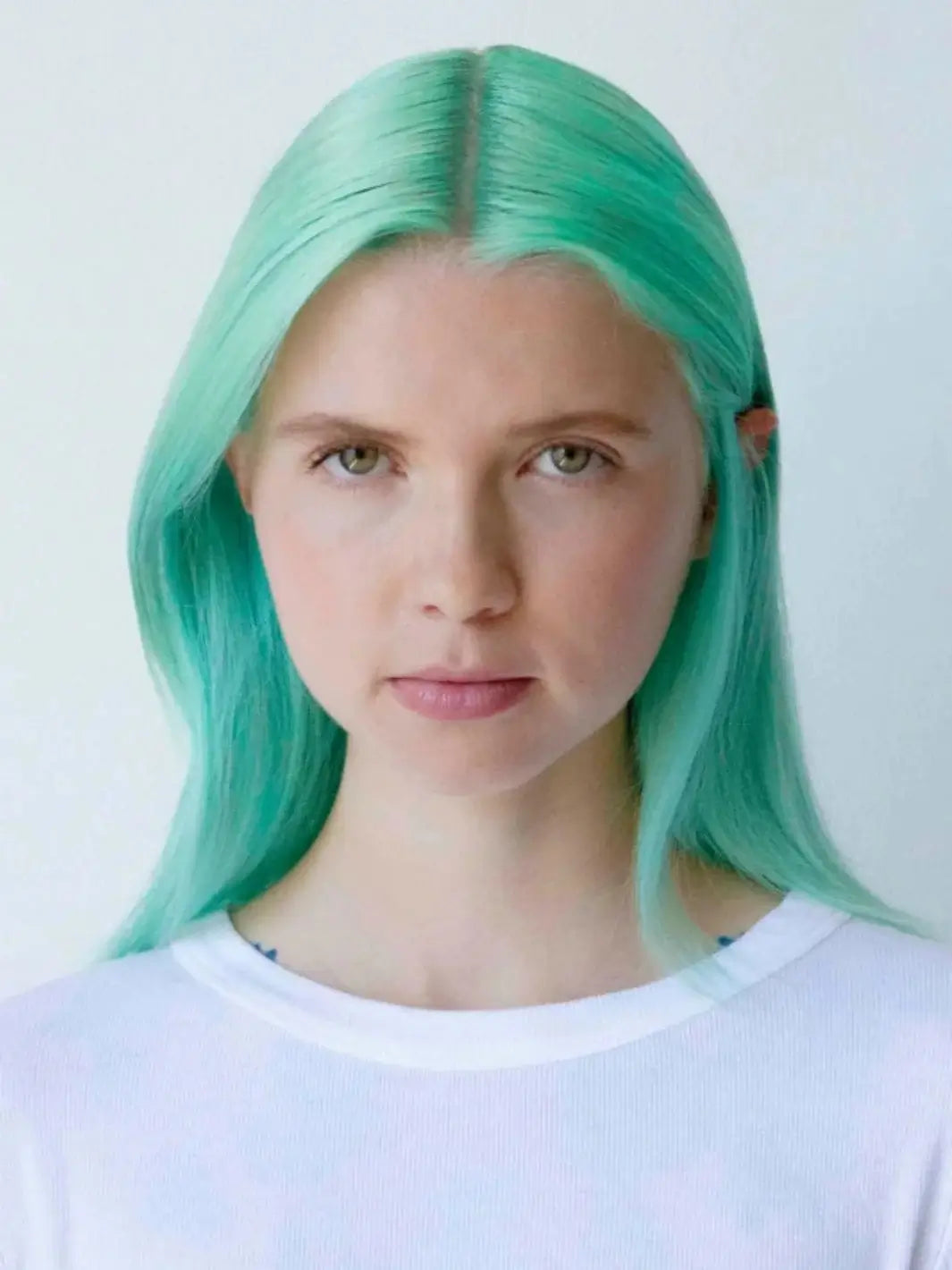 A front-facing headshot of a model with vibrant, mint green hair maintained with R+Co GEMSTONE ChromoHance Color Shampoo | Twentyseven Toronto