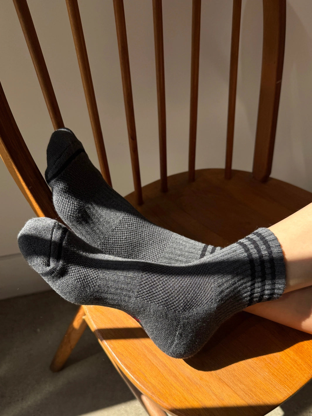 Le Bon Shoppe Girlfriend Socks in Soot with black contrast stripes, styled in sunlight on a wooden chair | Twentyseven Toronto