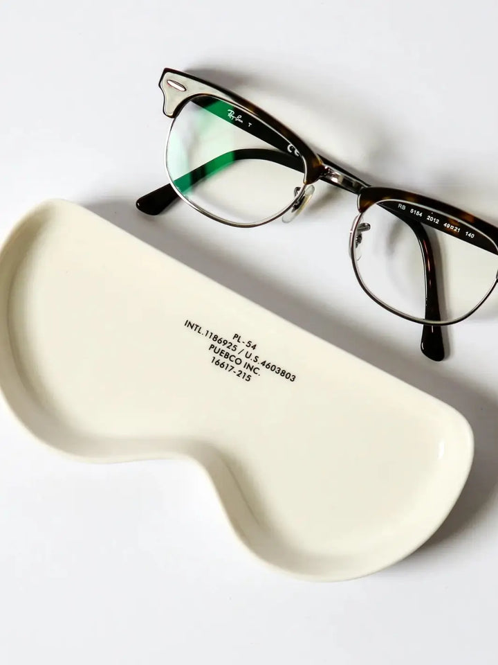 A pair of classic half-rim eyeglasses sits next to an empty white ceramic Glasses Tray - Round from Puebco | Twentyseven Toronto