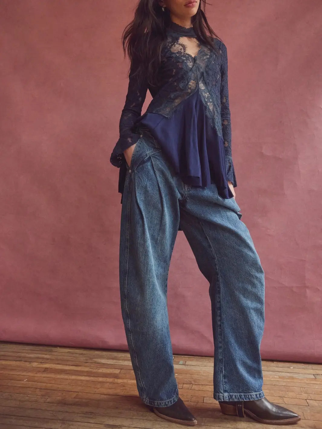 Full-length front shot of a model styled in the Free People We the Free Golden Hour Trouser Jeans in Deacon Blue with a lace top against a pink studio backdrop | Twentyseven