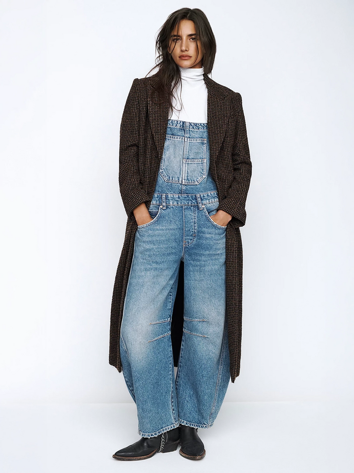 A front perspective captures a model posing with hands in pockets, wearing a plaid overcoat and the Free People Good Luck Overall in Ultra Light Beam  | Twentyseven Toronto