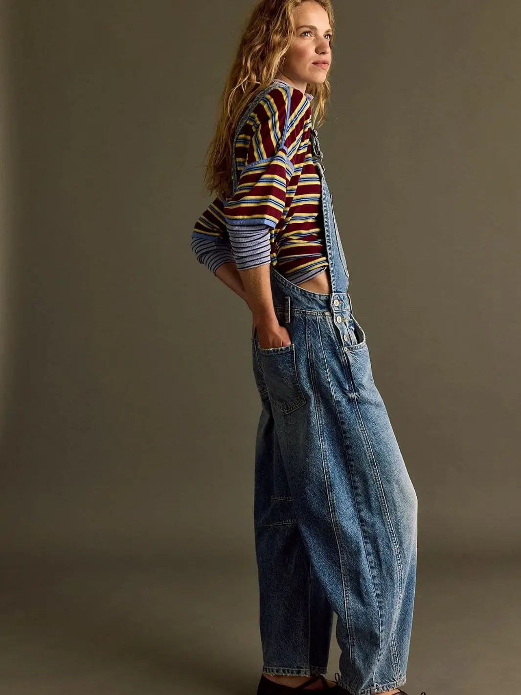 A side-angle studio portrait showcases the slouchy, comfortable fit of the Free People Good Luck Overall in Ultra Light Beam layered over a striped t-shirt | Twentyseven Toronto