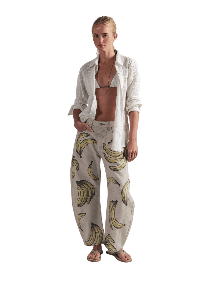 A model wearing the Free People Good Luck Printed Barrel Jeans in Go Bananas with an open white shirt and sandals | Twentyseven Toronto