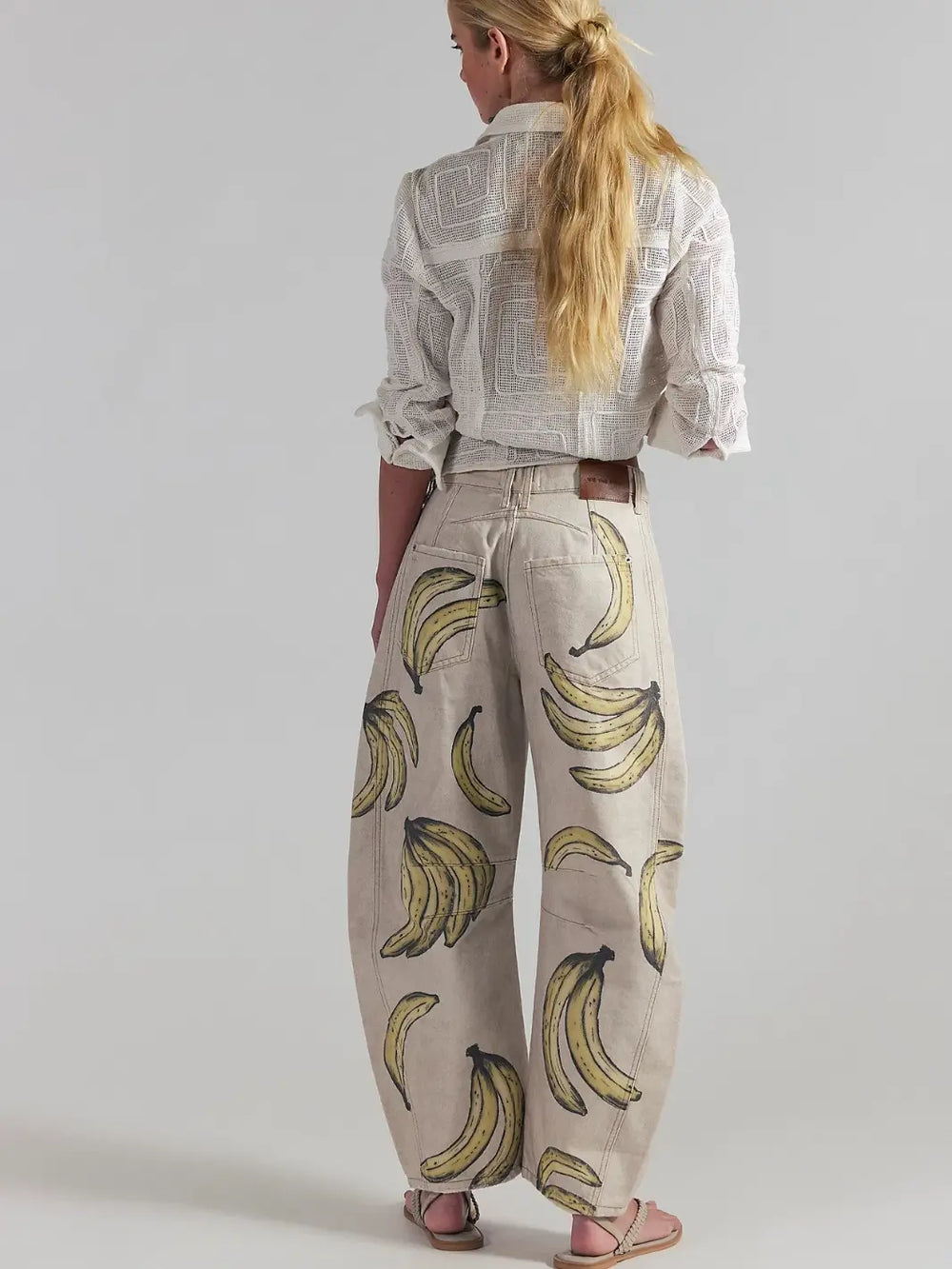 A rear full-length view of a model wearing a white textured shirt and the Free People Good Luck Printed Barrel Jeans in Go Bananas | Twentyseven Toronto
