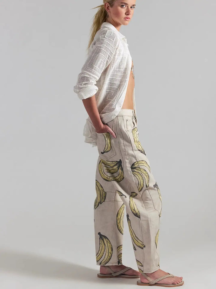 A side-profile view of a model standing in a white unbuttoned shirt and the Free People Good Luck Printed Barrel Jeans in Go Bananas | Twentyseven Toronto