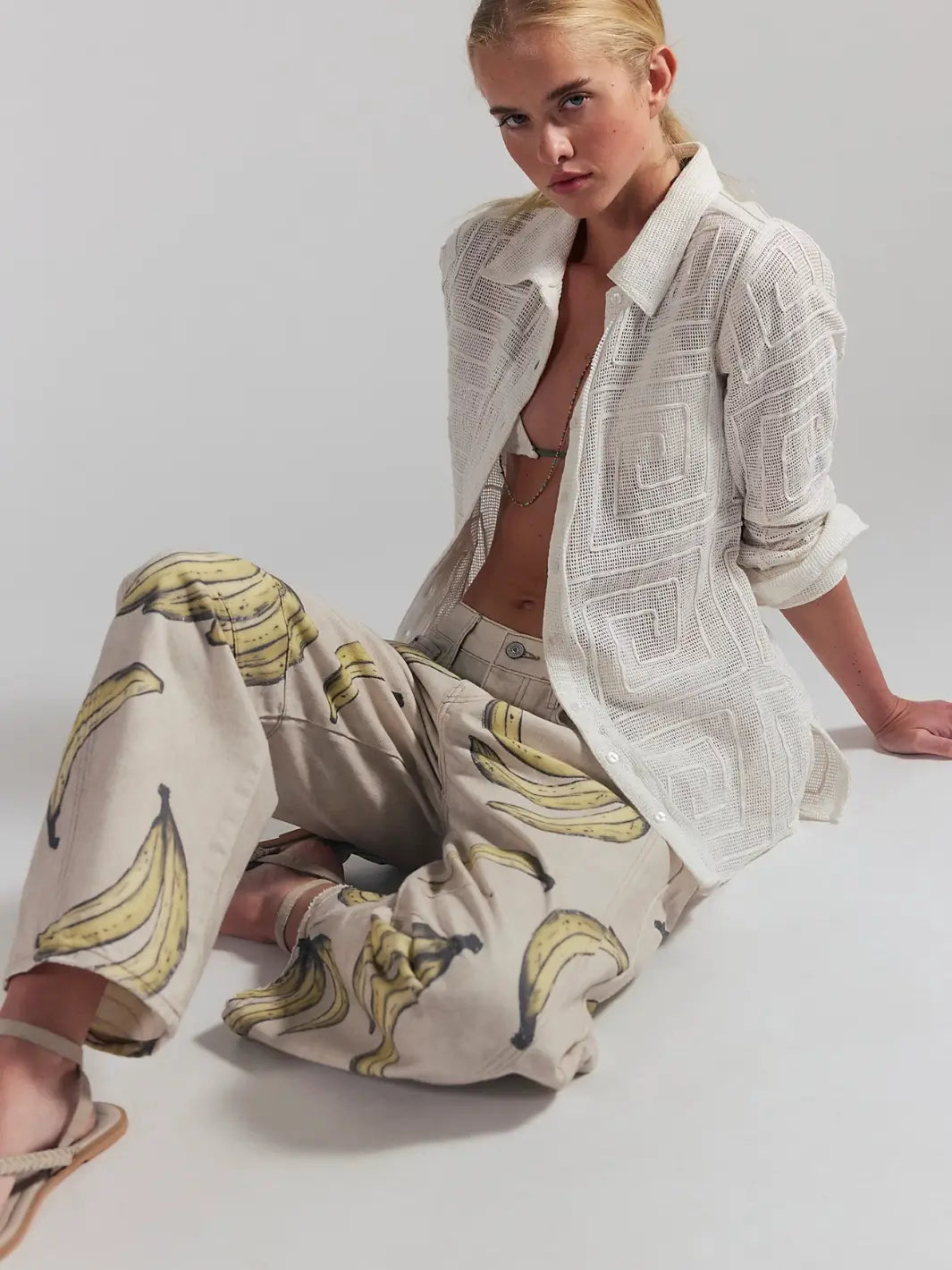 A model sits on the floor while wearing an open white textured long-sleeve shirt and the Free People Good Luck Printed Barrel Jeans in Go Bananas | Twentyseven Toronto