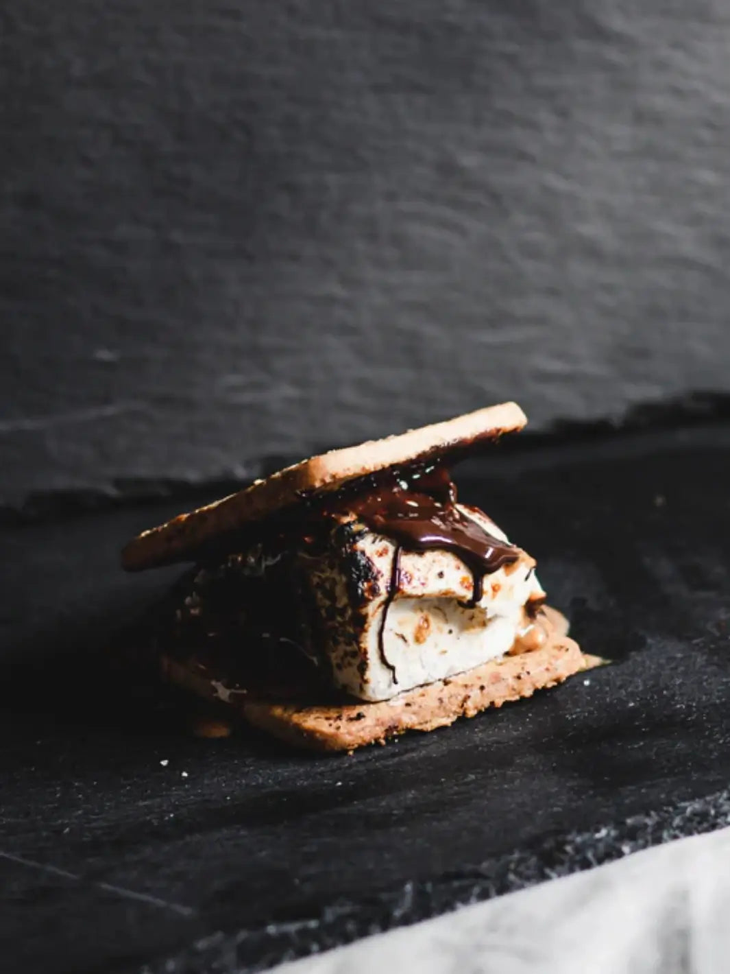 A decadent s'more featuring a perfectly toasted marshmallow and melting chocolate sauce between graham crackers, showcasing a finished treat from the Mojave Mallows Gourmet S'mores Kit | Twentyseven Toronto