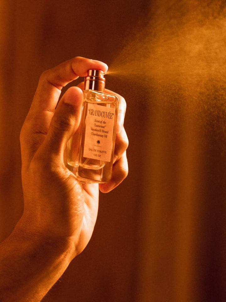 "GRAND CUVÉE" by Vacation Inc Eau de Toilette | Twentyseven Toronto | Hand holding a small bottle labeled 'Grand Cuvée' against a warm, blurred background