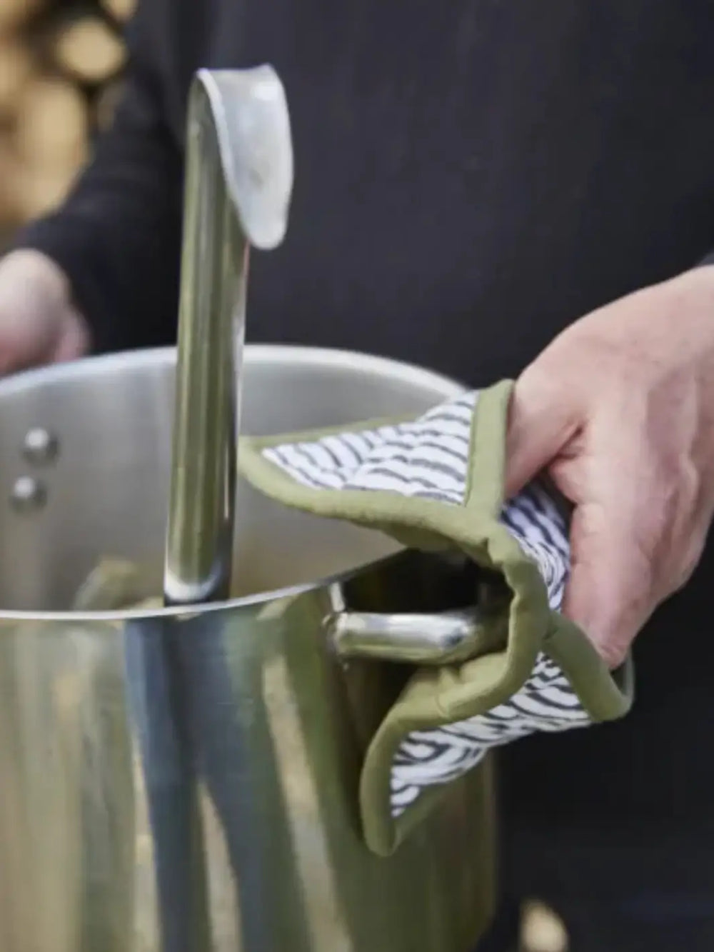 Person holding a pot with a olive green and white striped oven mitt from Sylvie Thiriez | Twentyseven Toronto