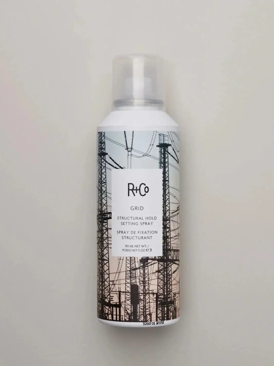 An aerosol bottle of R+Co GRID Structural Hold Setting Spray stands upright against a plain, neutral grey background | Twentyseven Toronto
