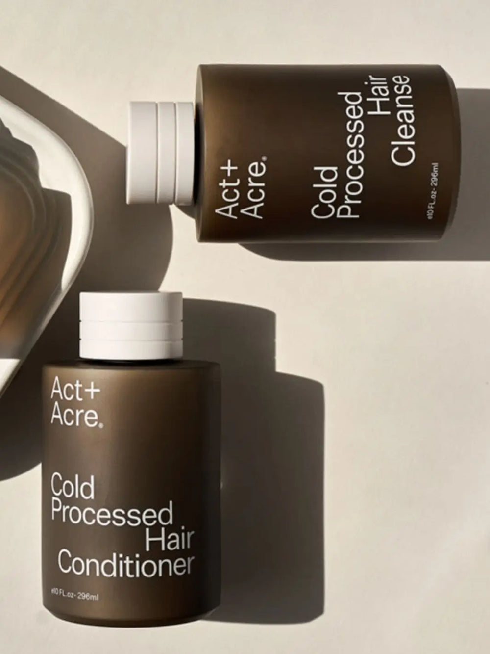 Two bottles of Act+Acre Cold Processed Hair Cleanse and Conditioner on a neutral background | Twentyseven Toronto