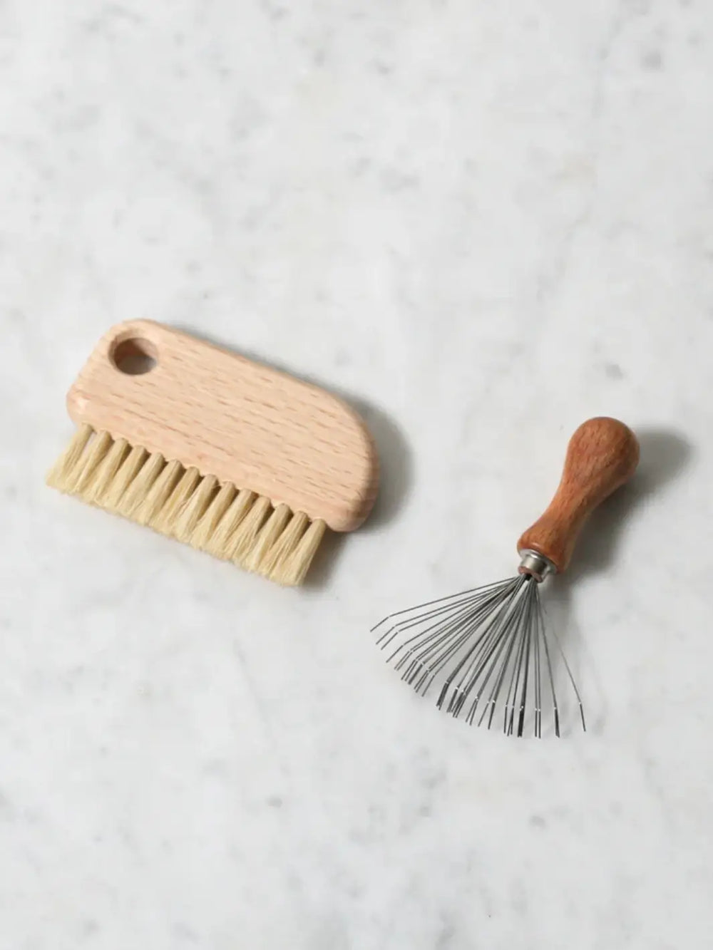 Wooden brush and metal rake from Burstenhaus Redecker on a marble surface | Twentyseven Toronto