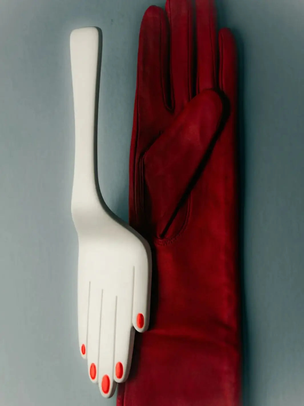 White hand-shaped cake server with red nail polish beside a deep red glove from Maison Balzac on a gray background | Twentyseven Toronto