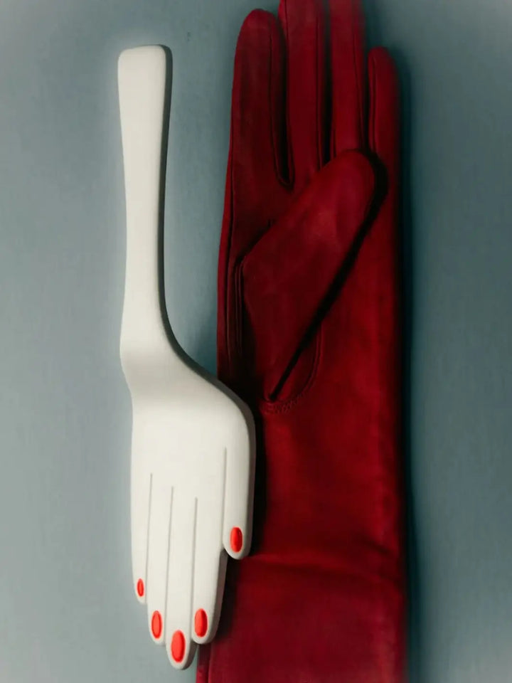 White hand-shaped cake server with red nail polish beside a deep red glove from Maison Balzac on a gray background | Twentyseven Toronto