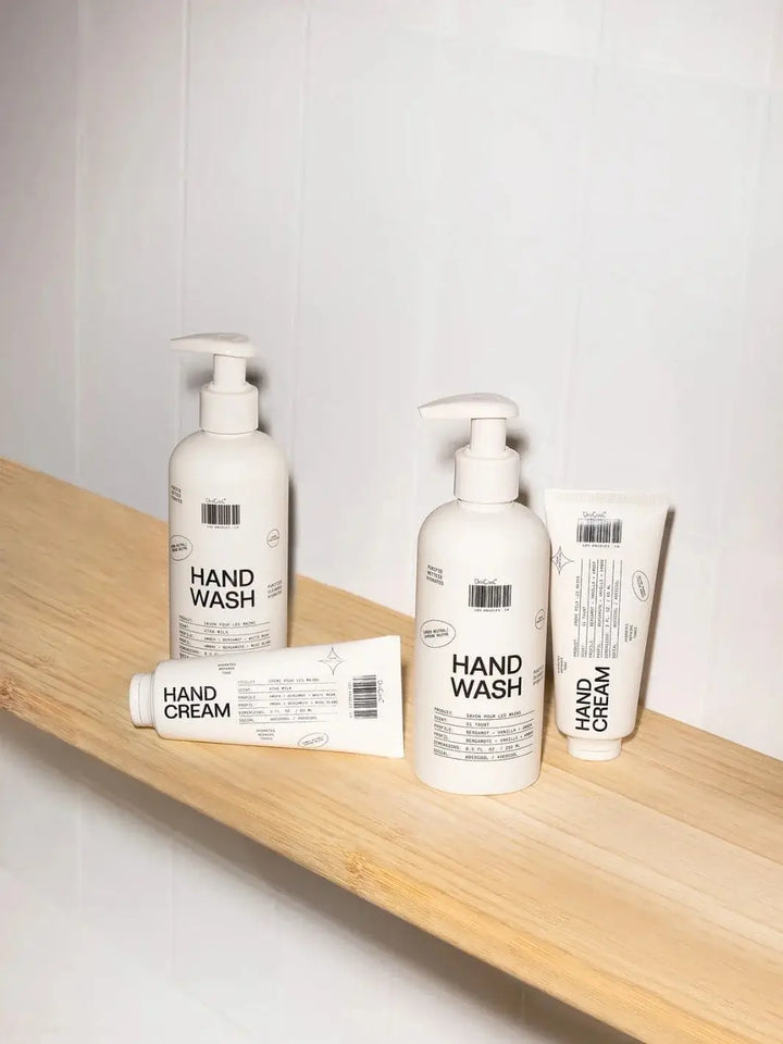 Two bottles of Dedcool Hand Wash Xtra Milk and two tubes of matching hand cream are arranged on a light wooden shelf against a white tiled wall | Twentyseven Toronto