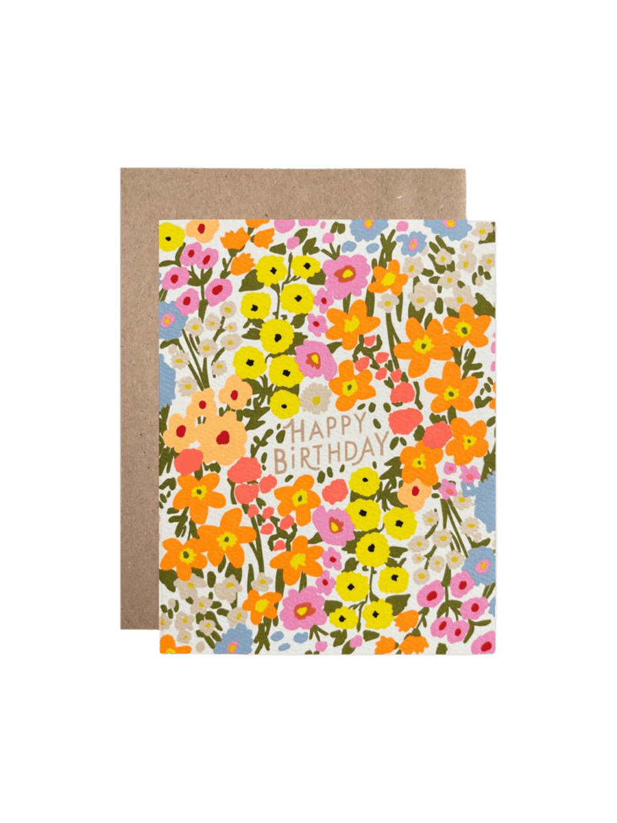 The Hartland Cards Happy Birthday Anna's Garden Card features a dense, vibrant pattern of illustrated wildflowers in shades of yellow, orange, pink, and light blue, with the words "HAPPY BIRTHDAY" printed in a soft tan font in the center, paired with a brown kraft envelope | Twentyseven