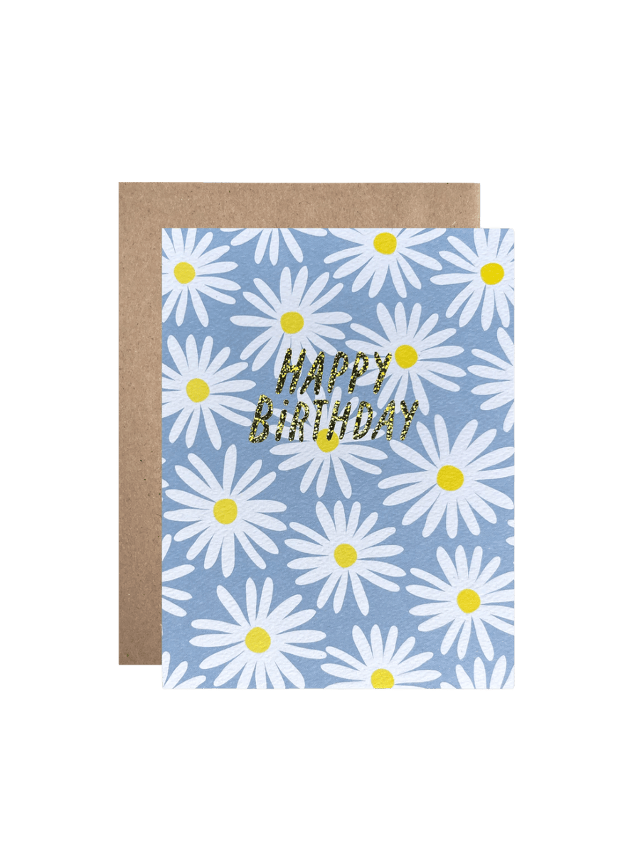 The Happy Birthday Daisies Card from Hartland Cards features a repeating pattern of white daisies with yellow centers on a light blue background, paired with a brown kraft envelope and glittering gold text | Twentyseven Toronto