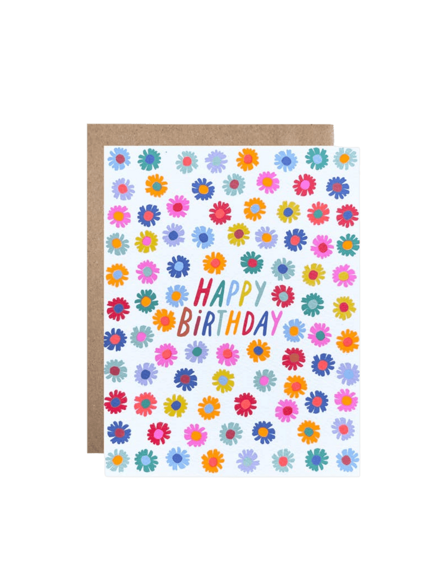 The Hartland Cards Happy Birthday Darling Daisies Card features a white background decorated with a dense, repeating pattern of small illustrated daisies in a vibrant mix of pink, orange, yellow, blue, red, and purple. In the center, the words "HAPPY BIRTHDAY" are written in a playful, multi-colored font, paired with a brown kraft envelope | Twentyseven