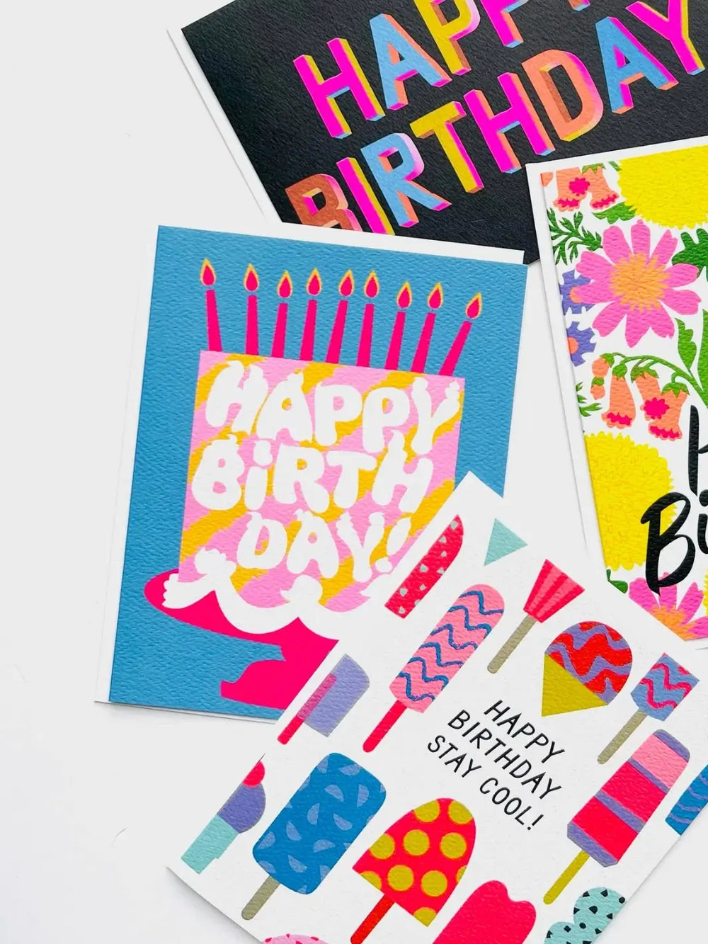 An angled flat lay on a white background shows the Banquet Workshop Happy Birthday Pink Cake Dreams Note Card arranged alongside other colorful, illustrated birthday cards | Twentyseven