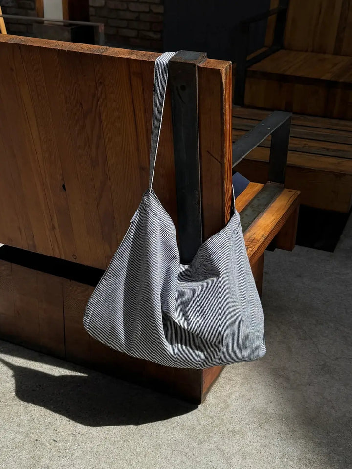 Le Bon Shoppe Happy Carry Tote Bag in 'Blue Stripe' design hanging on a wooden bench outdoors | Twentyseven Toronto