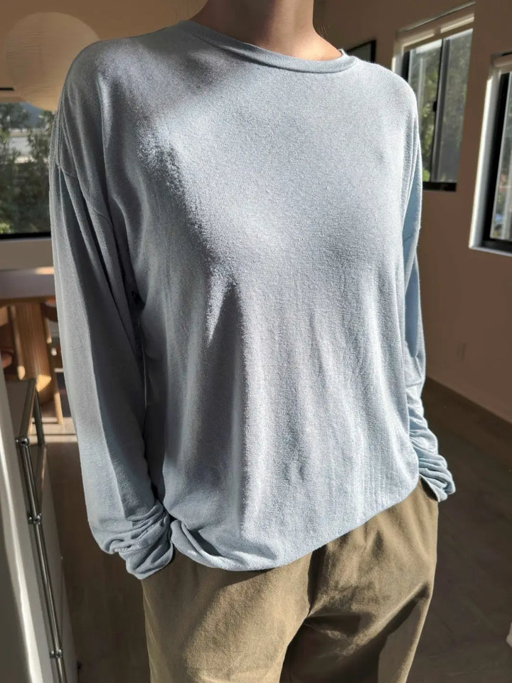 Person wearing a baby blue long-sleeve 'Haze Linen Blend Tee' shirt in 'Moonbeam' and dark green pants from Le Bon Shoppe in an indoor setting | Twentyseven Toronto