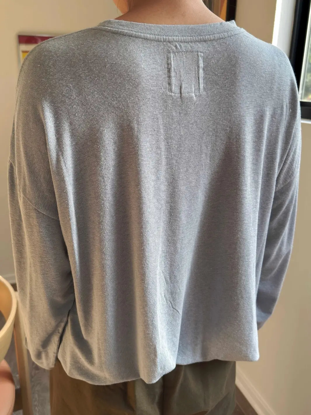 Back view of person wearing a baby blue long-sleeve 'Haze Linen Blend Tee' shirt in 'Moonbeam' from Le Bon Shoppe against a neutral background | Twentyseven Toronto