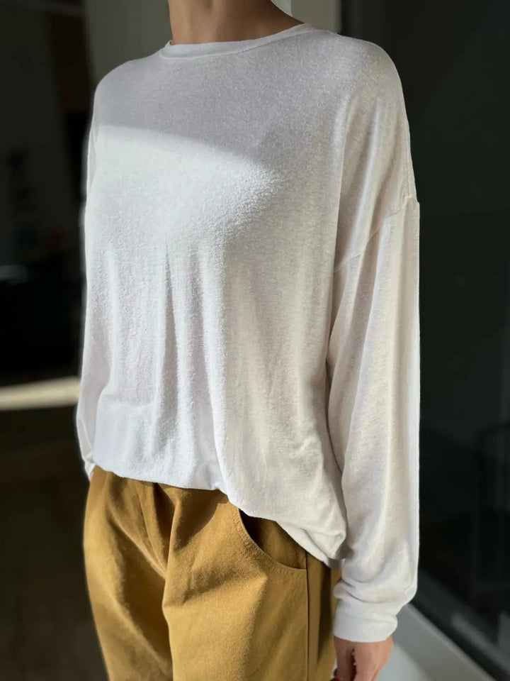 Person wearing a white long-sleeve 'Haze Linen Blend Tee' shirt and mustard yellow pants from Le Bon Shoppe against a blurred background | Twentyseven Toronto