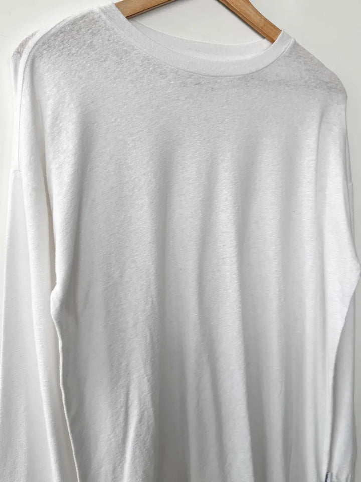 Close up of white long-sleeve 'Haze Linen Blend Tee' shirt from Le Bon Shoppe on a wooden hanger against a white background | Twentyseven Toronto