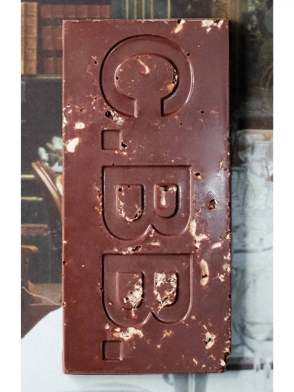 Close-up of the Hazelnut Butter 74% Chocolate Bar from Casa Bosques showing the dark chocolate surface embossed with "C.B.B." and filled with visible pieces of crushed hazelnuts | Twentyseven Toronto