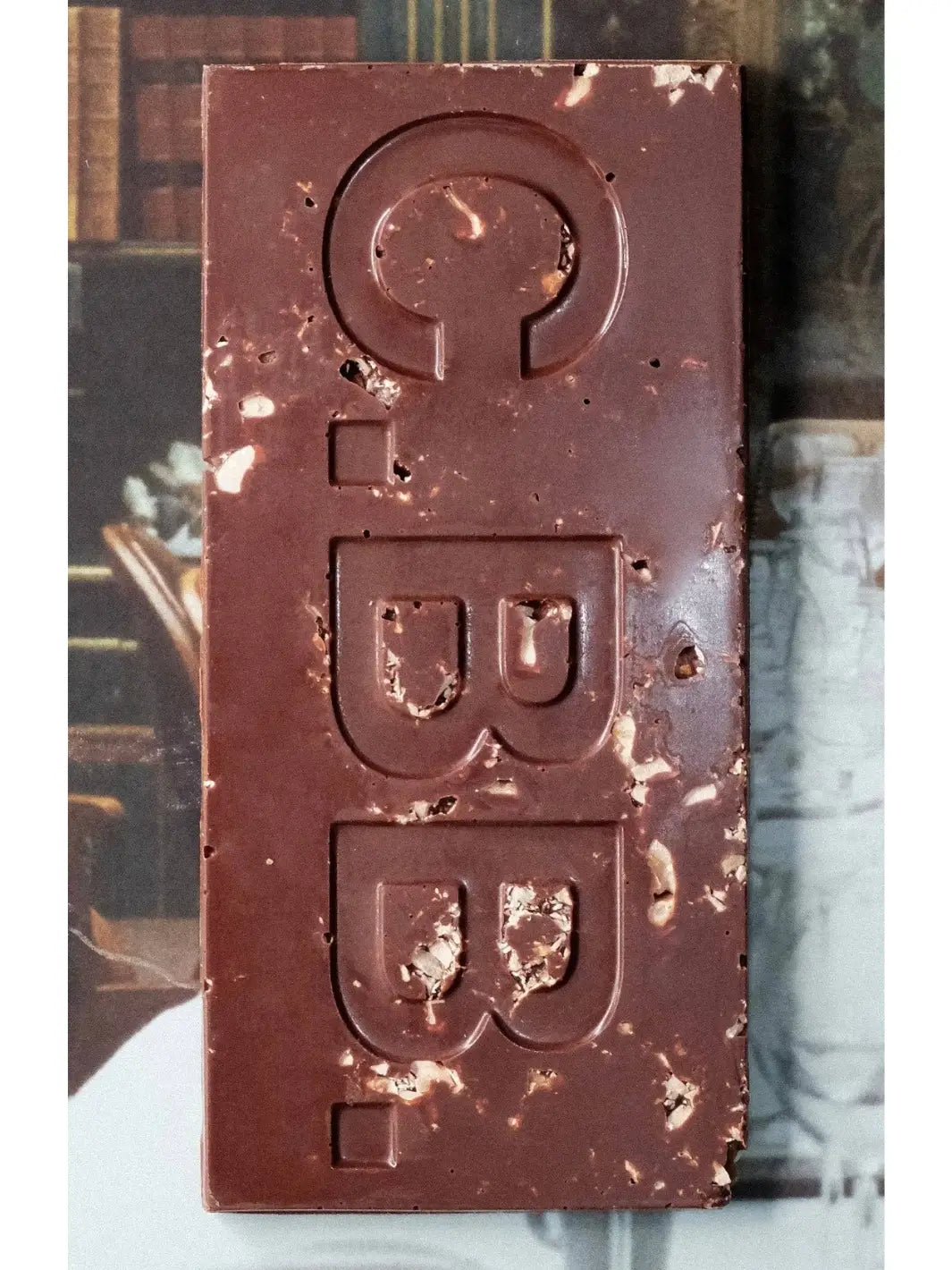 Close-up of the Hazelnut Butter 74% Chocolate Bar from Casa Bosques showing the dark chocolate surface embossed with "C.B.B." and filled with visible pieces of crushed hazelnuts | Twentyseven Toronto