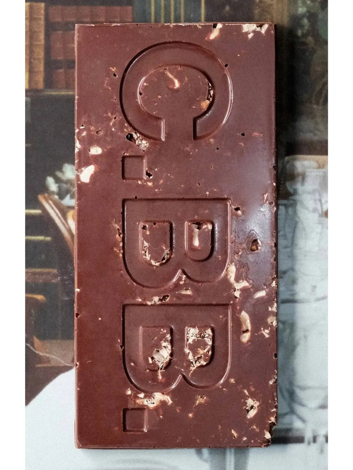 Close-up of the Hazelnut Butter 74% Chocolate Bar from Casa Bosques showing the dark chocolate surface embossed with "C.B.B." and filled with visible pieces of crushed hazelnuts | Twentyseven Toronto