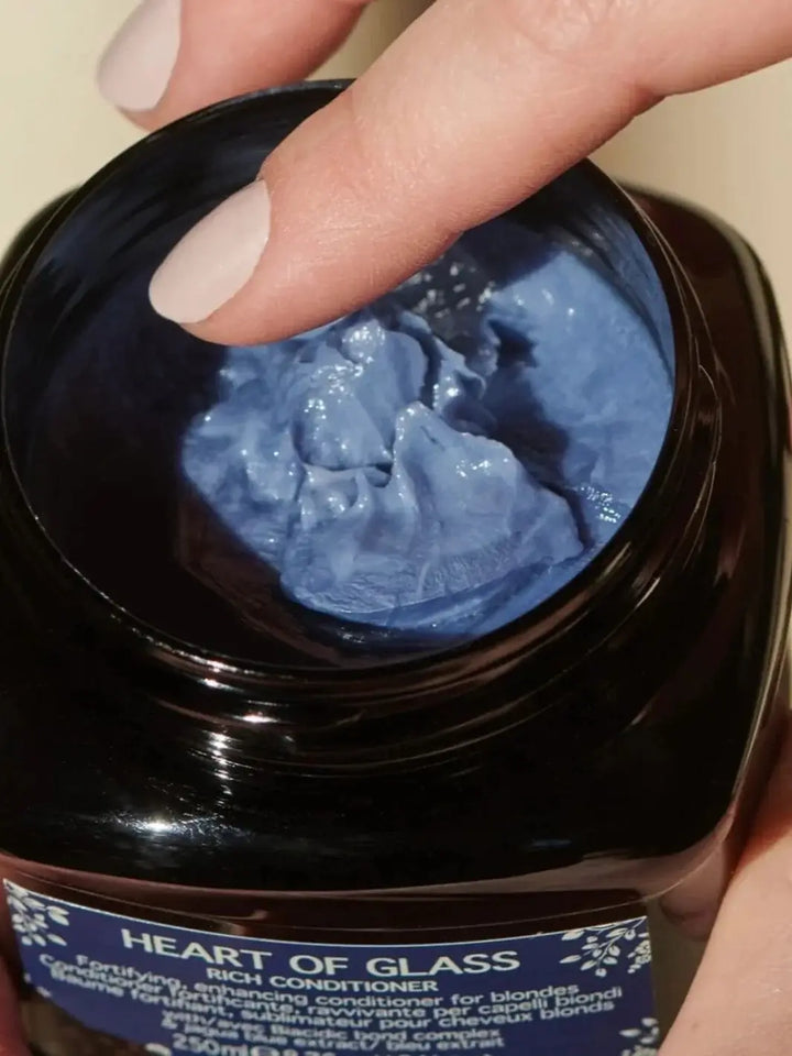 A close-up view shows a finger touching the thick, textured blue cream inside an open jar of Davines Heart of Glass Rich Conditioner | Twentyseven Toronto
