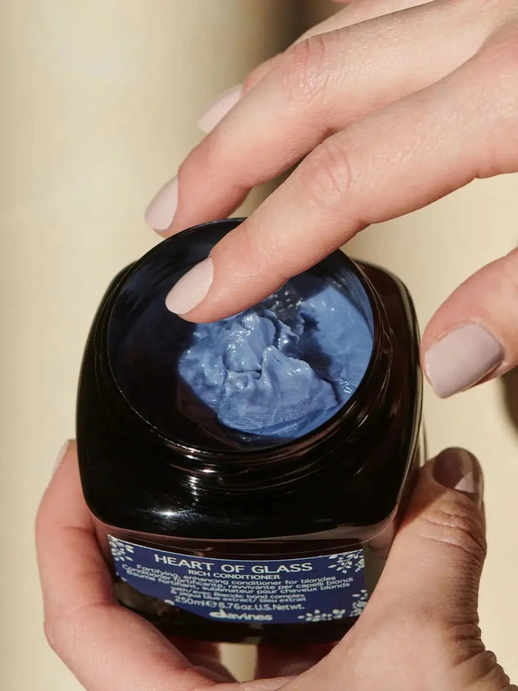 A close-up view shows a finger touching the thick, textured blue cream inside an open jar of Davines Heart of Glass Rich Conditioner | Twentyseven Toronto