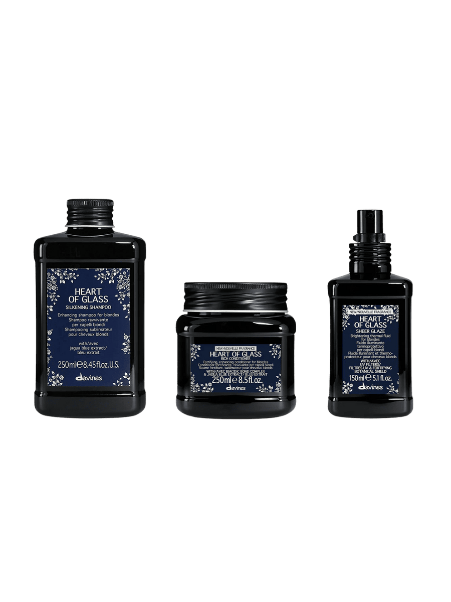 Three black bottles from Davines with blue labels including Heart of Glass Silkening Shampoo, Heart of Glass Silkening Conditioner and Heart of Glass Sheer Glaze on a transparent background | Twentyseven Toronto