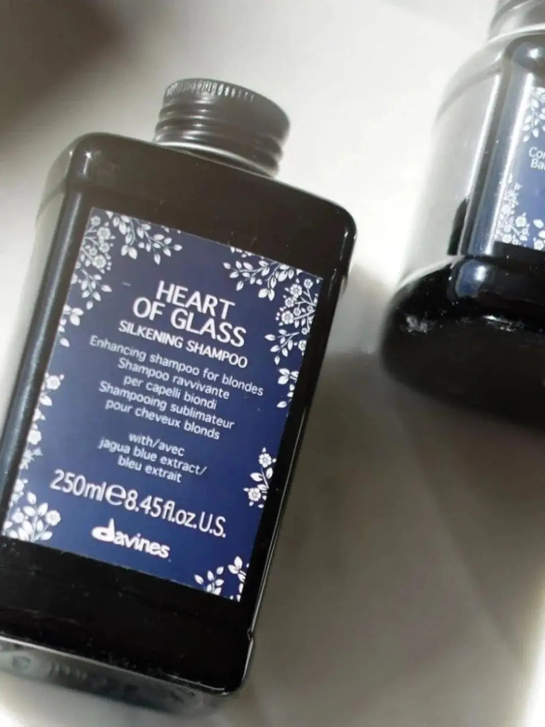 A dark bottle of Davines Heart of Glass Silken Shampoo sits at an angle next to another bottle | Twentyseven Toronto
