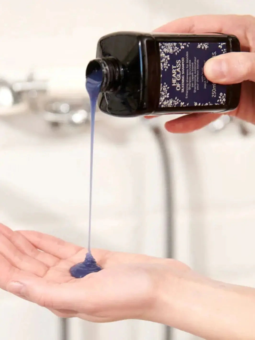 A thick, dark blue liquid pours from an inverted bottle of Davines Heart of Glass Silken Shampoo onto an open palm | Twentyseven Toronto