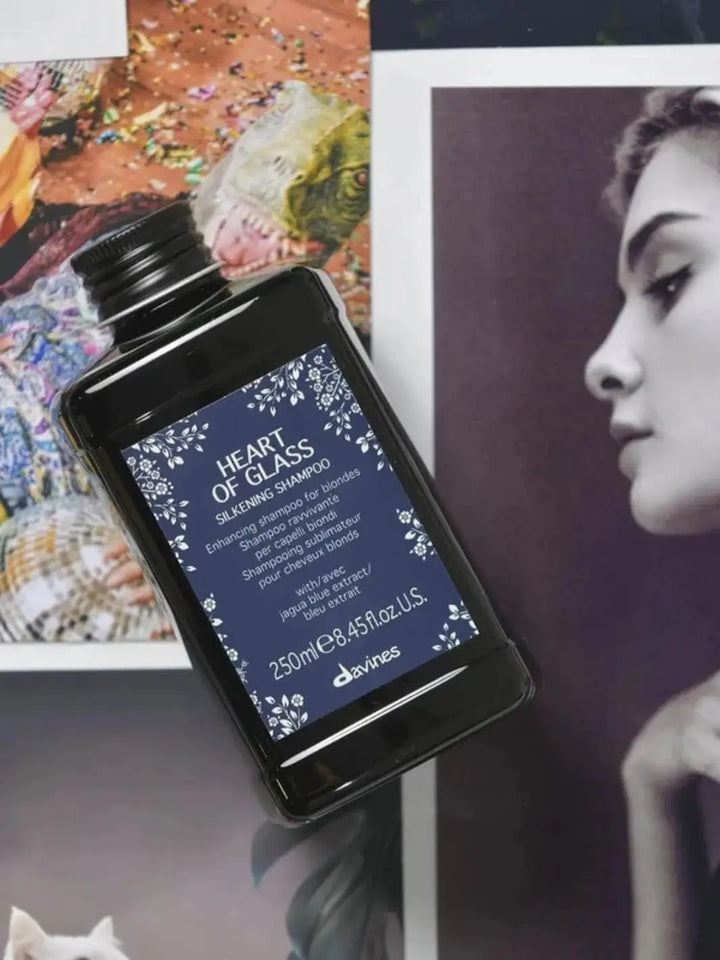 A dark rectangular bottle of Davines Heart of Glass Silkening Shampoo is positioned diagonally across a collection of printed photographs | Twentyseven Toronto