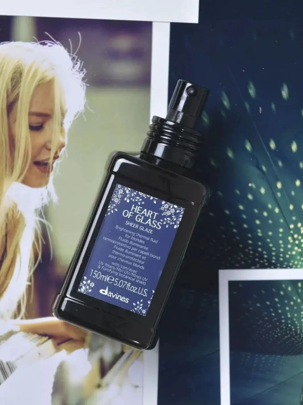 A dark bottle of Davines Heart of Glass Sheer Glaze rests at an angle on top of printed photographs, including one of a blonde woman | Twentyseven Toronto
