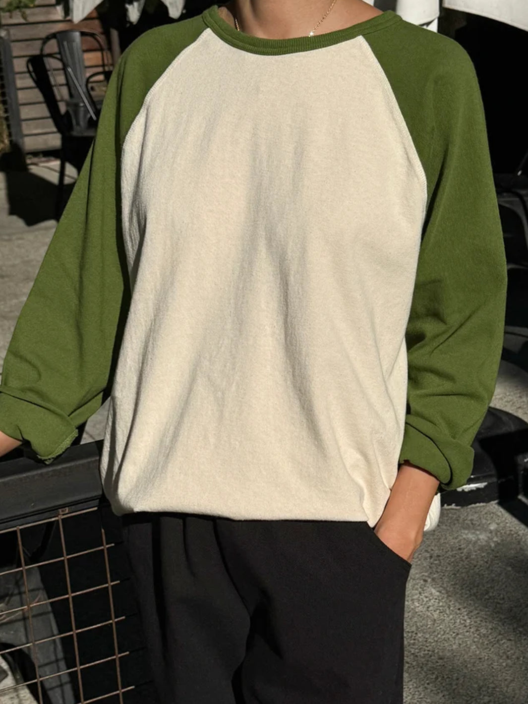 Model wearing Heavy Cotton Raglan Tee in Naturel/Collard Green with a cream body, green raglan sleeves and ribbed crew neckline, styled with black relaxed-fit pants | Twentyseven Toronto