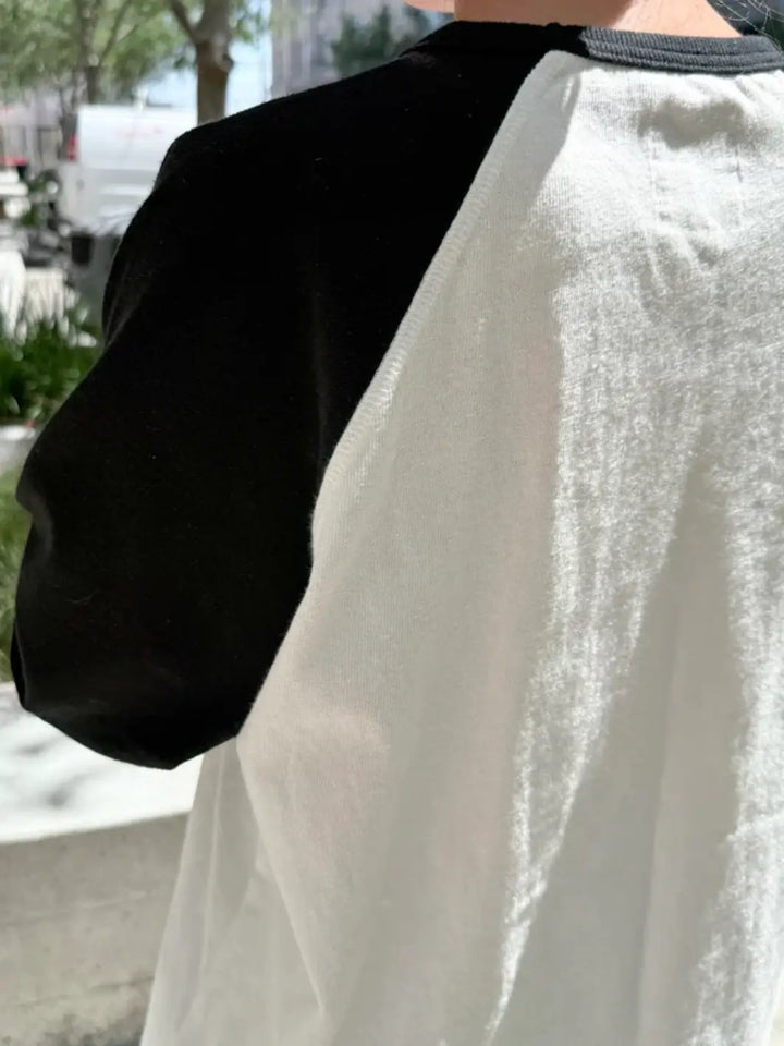 An outdoor side-angle shot showcases the textured knit fabric and the contrasting raglan sleeve seam of the Le Bon Shoppe Heavy Cotton Raglan Tee in White/Black | Twentyseven Toronto