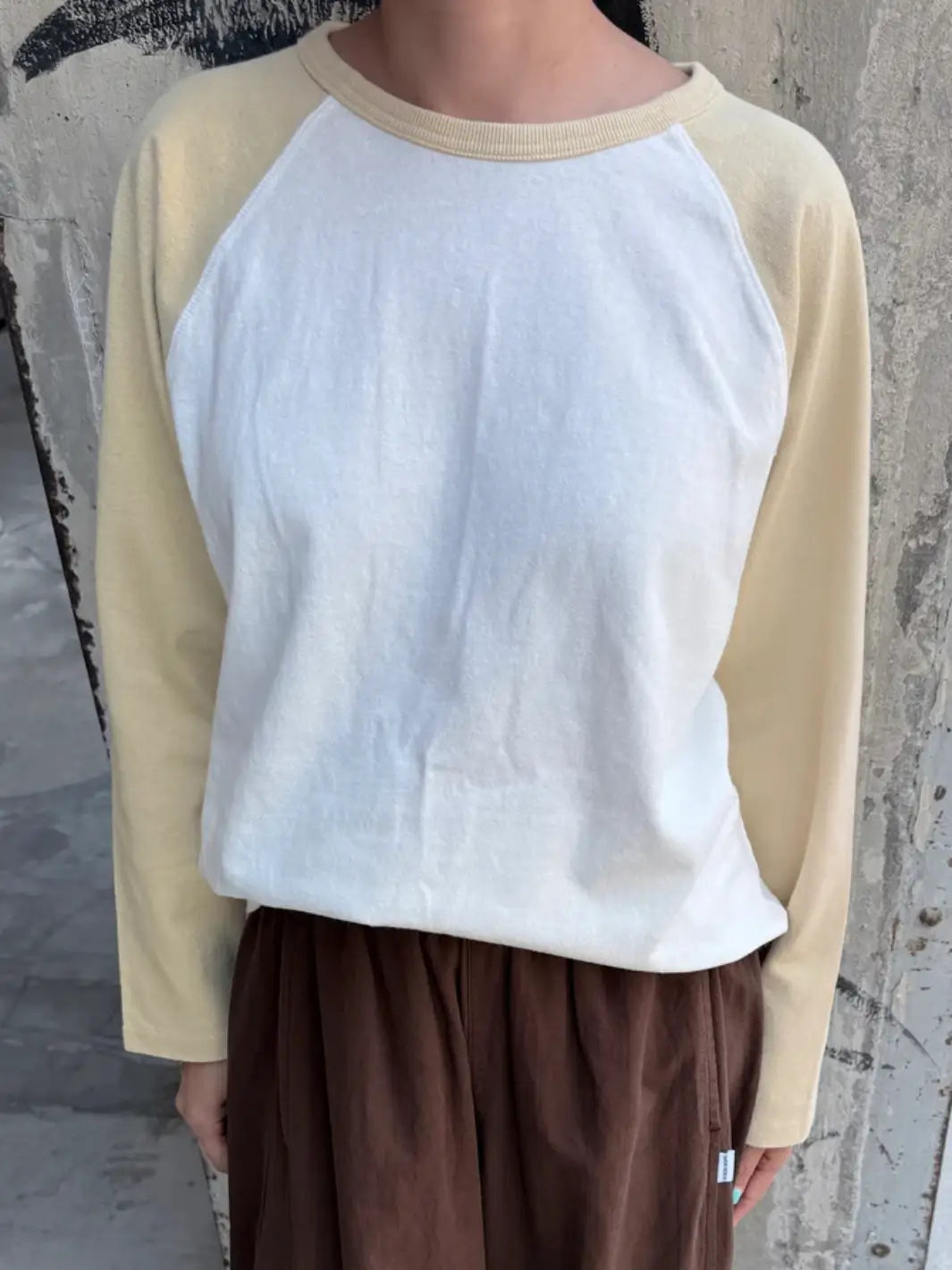 A front view shows a model wearing the white and yellow Le Bon Shoppe Heavy Cotton Raglan Tee in White/Butter paired with casual dark brown pants | Twentyseven Toronto