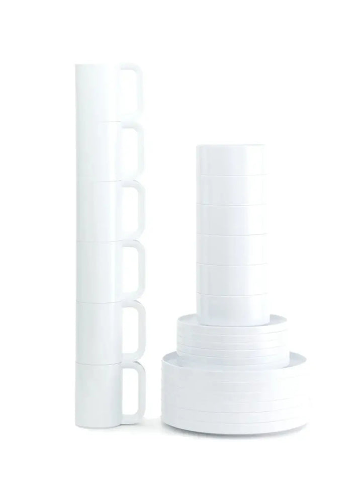 A vertical stack of white mugs beside stacked white bowls and plates from the Heller Max Dinnerware Collection in White - Set of 6 against a white backdrop | Twentyseven Toronto