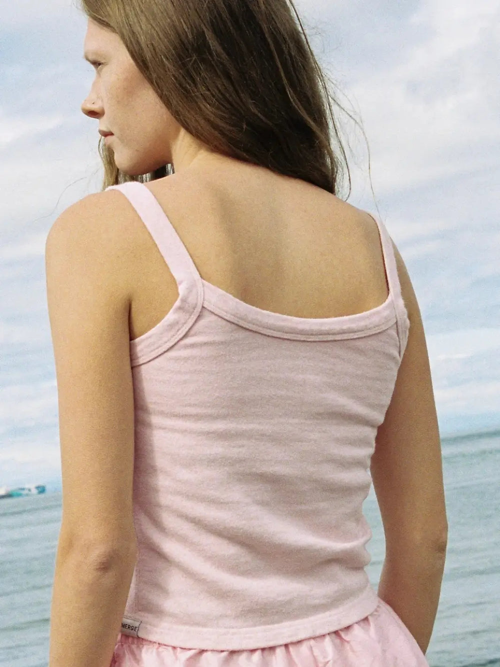 A back view of the scoop-back design and thick shoulder straps of the light pink Merge Goods Hemp Breeze Tank Top in Pink Cream worn at the beach | Twentyseven Toronto