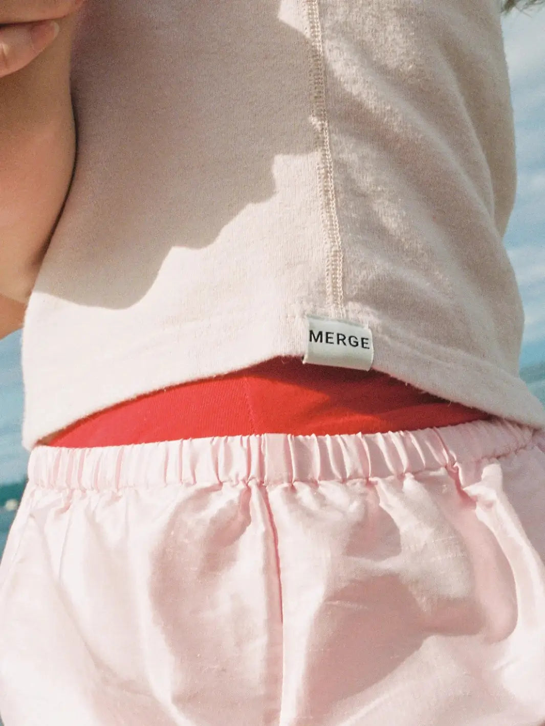 A close-up focuses on the small white brand label stitched onto the bottom hem of the light pink Merge Goods Hemp Breeze Tank Top in Pink Cream | Twentyseven Toronto