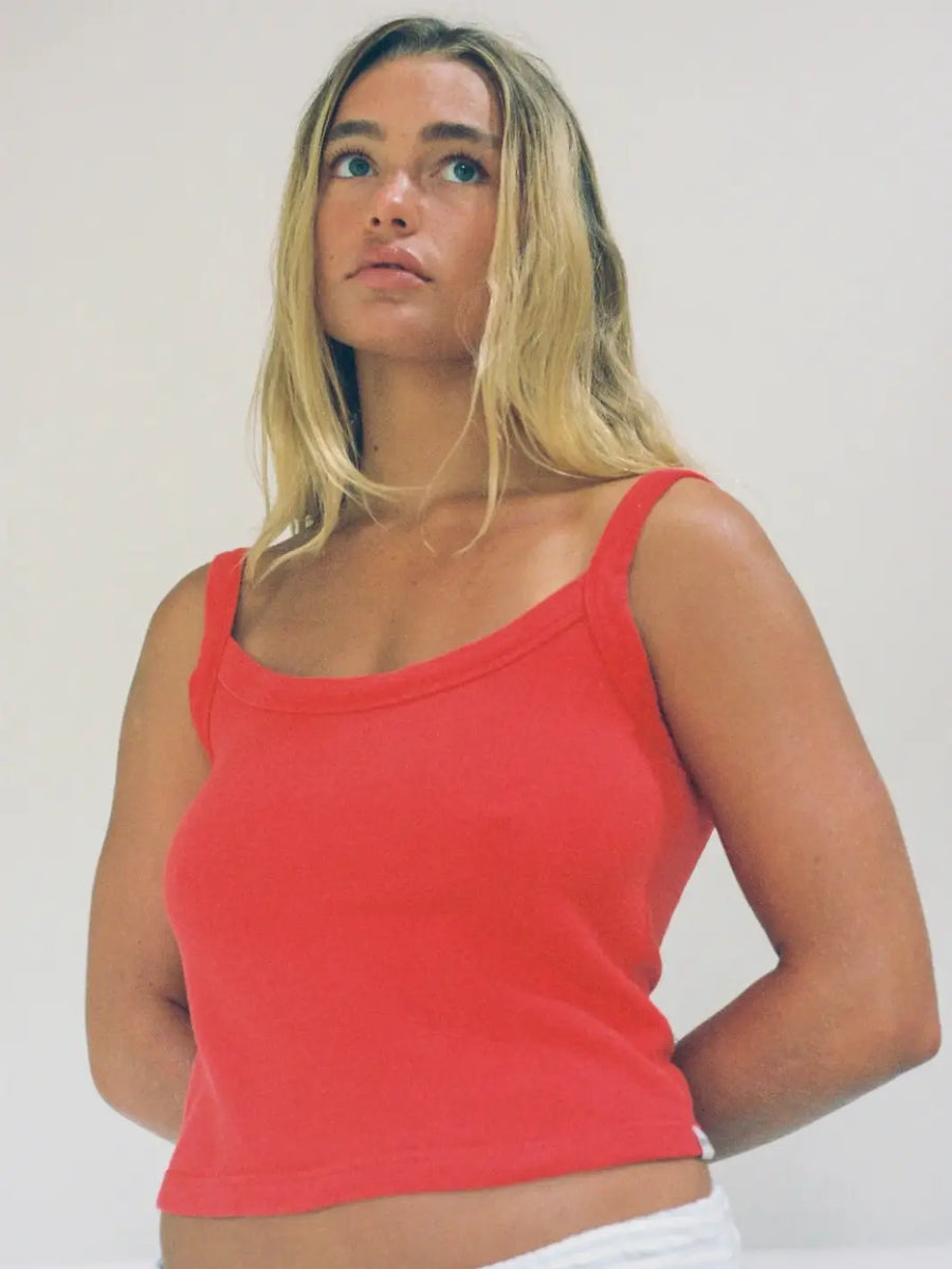 Blonde woman looking upwards while wearing the vibrant red Merge Goods Hemp Breeze Tank Top in Poppy Red with wide shoulder straps | Twentyseven Toronto