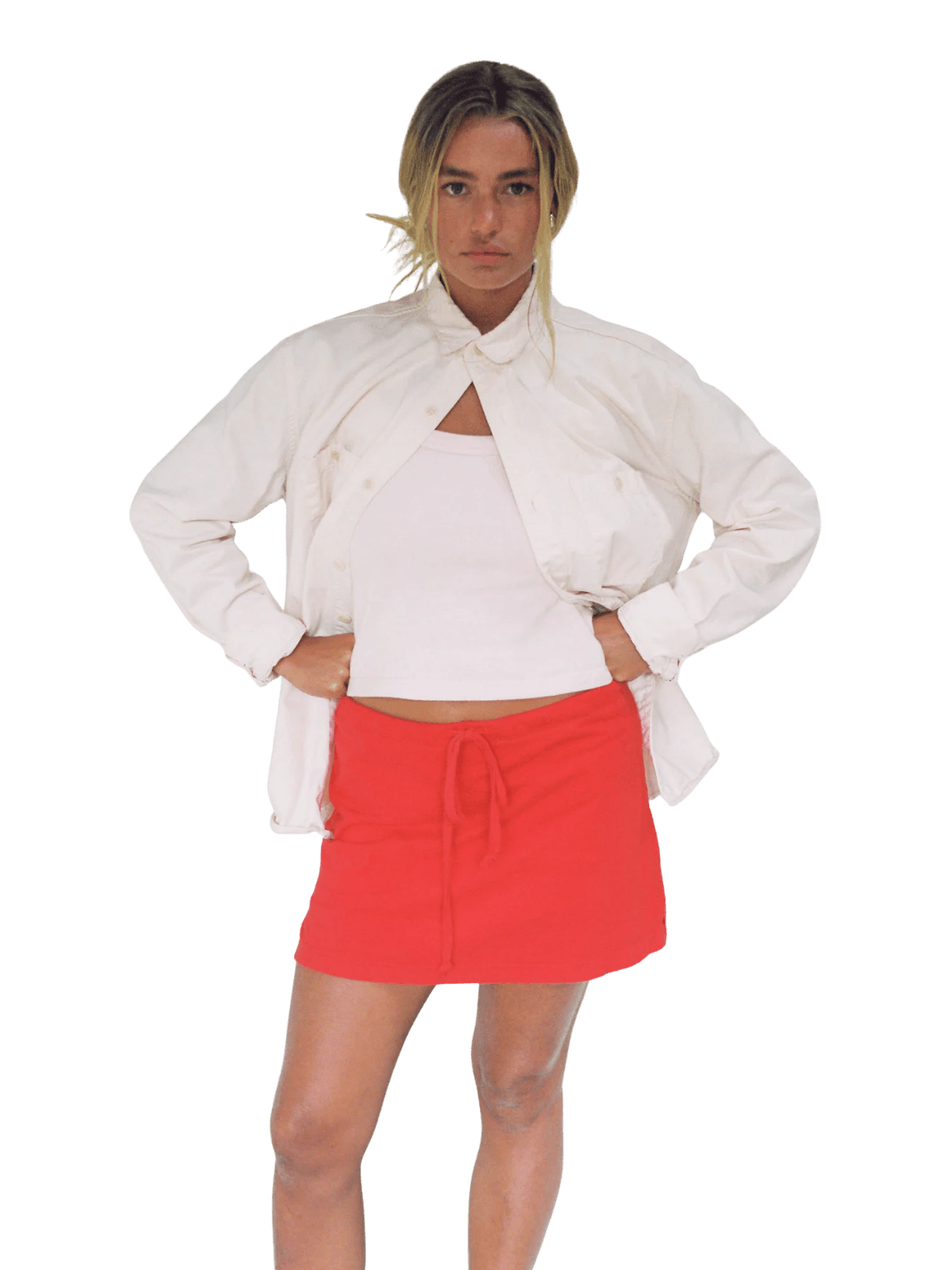 A model wearing the bright red Merge Goods Hemp Lazy Skort in Poppy Red under a white top and an open white button-down jacket | Twentyseven Toronto