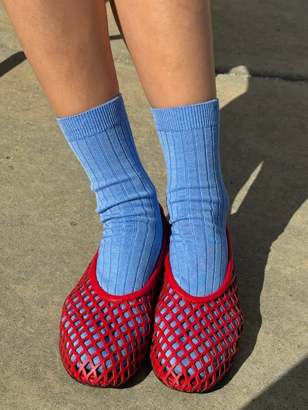 Person wearing blue Her Socks in 'Periwinkle' from Le Bon Shoppe and red mesh flats on a concrete floor | Twentyseven Toronto