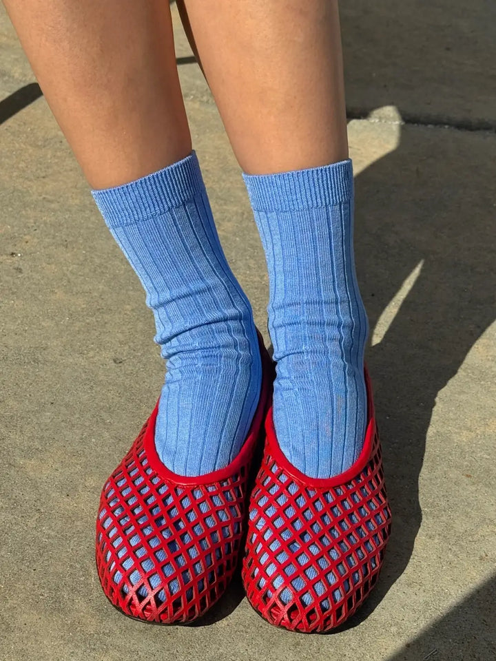 Person wearing blue Her Socks in 'Periwinkle' from Le Bon Shoppe and red mesh flats on a concrete floor | Twentyseven Toronto